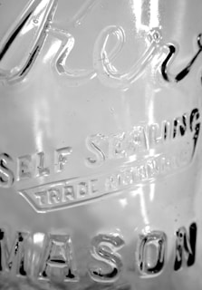 A close-up view of a glass surface featuring etched text that reads 'Self Sealing' and 'Mason'. The glass has a transparent appearance with light reflections and subtle texture visible on its surface.