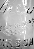 A close-up view of a glass surface featuring etched text that reads 'Self Sealing' and 'Mason'. The glass has a transparent appearance with light reflections and subtle texture visible on its surface.
