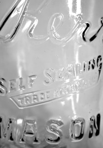 A close-up view of a glass surface featuring etched text that reads 'Self Sealing' and 'Mason'. The glass has a transparent appearance with light reflections and subtle texture visible on its surface.