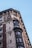 A detailed architectural facade of a historical building featuring ornate stone carvings, intricate cornices, and large windows with decorative frames. The structure primarily consists of red and beige bricks, accented by dark metal-windowed projections.