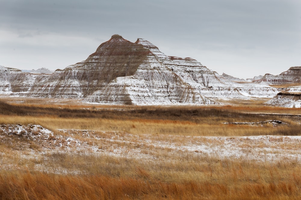 brown grass field near brown mountain under white sky during daytime