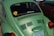 A green Volkswagen Beetle is parked next to a red car. The car displays a sticker on the rear window reading 'Powered by Love' with a peace sign and another message saying '0-60 Eventually!'. An Arizona license plate is visible with the number RTH1562.