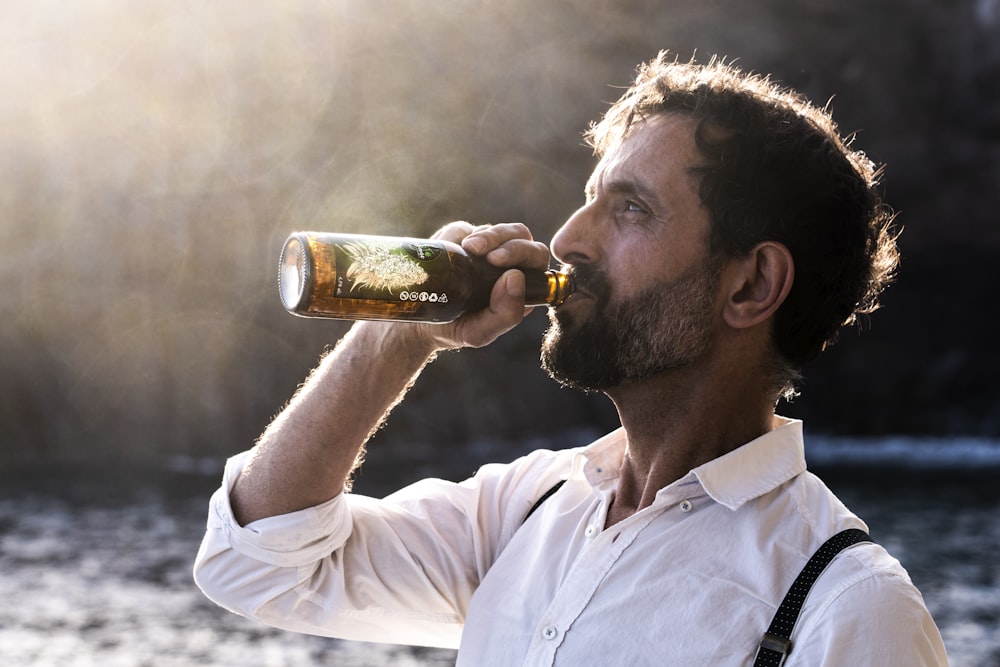 uomo in camicia bianca abbottonata che beve birra