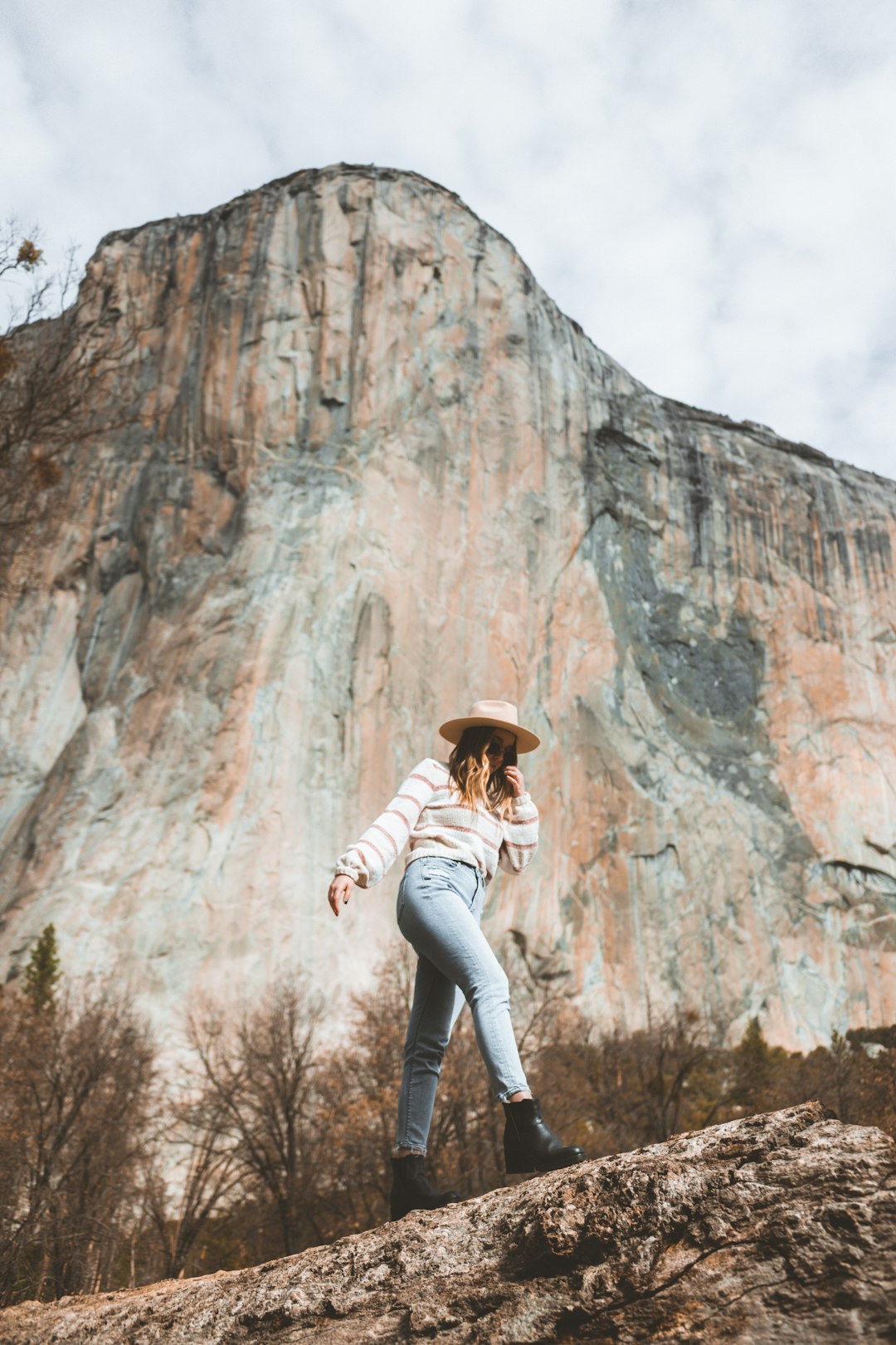 woman in white long sleeve shirt and white pants wearing brown hat standing near gray rock