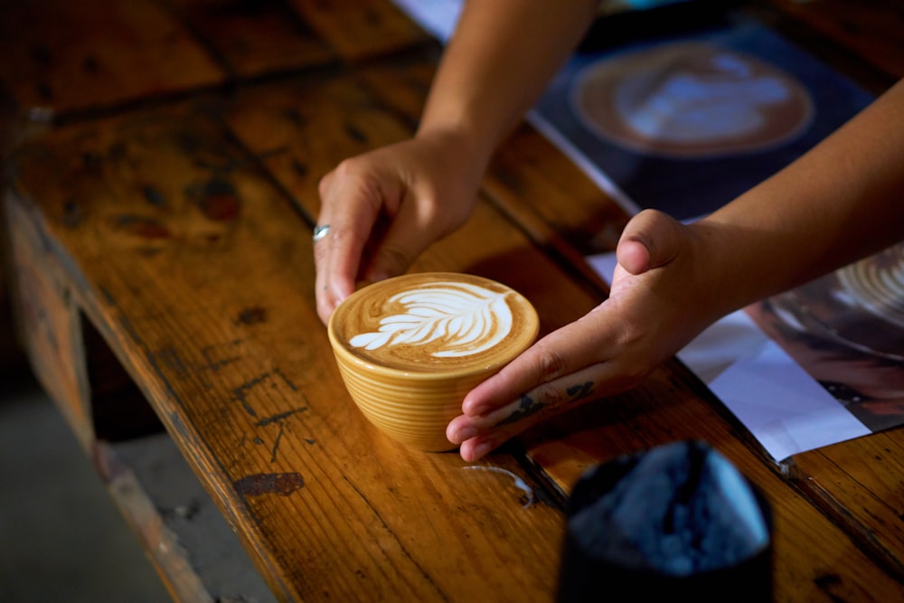 person holding cappuccino on brown wooden table