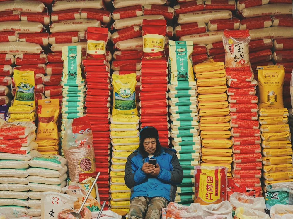 man in blue jacket sitting on red and yellow plastic packs