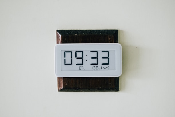 A sleek digital calendar clock mounted on a modern office wall, displaying time, date, and temperature clearly.