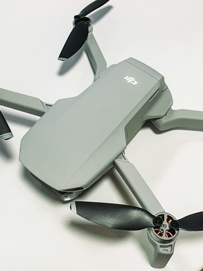 A compact, modern drone with a sleek grey body and four black propellers. The drone is positioned on a light surface, showcasing its aerodynamic design.