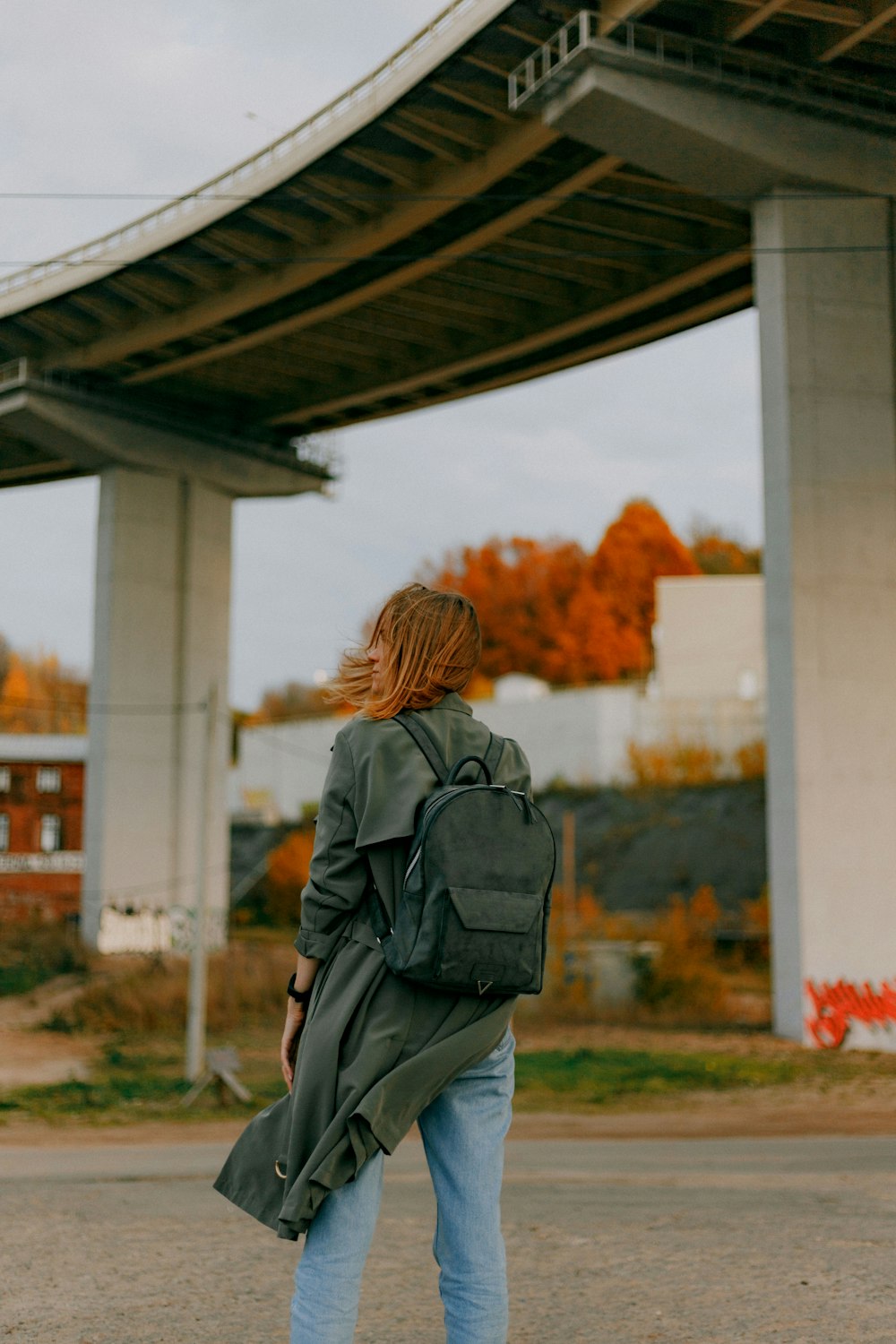 woman in gray jacket standing near bridge during daytime