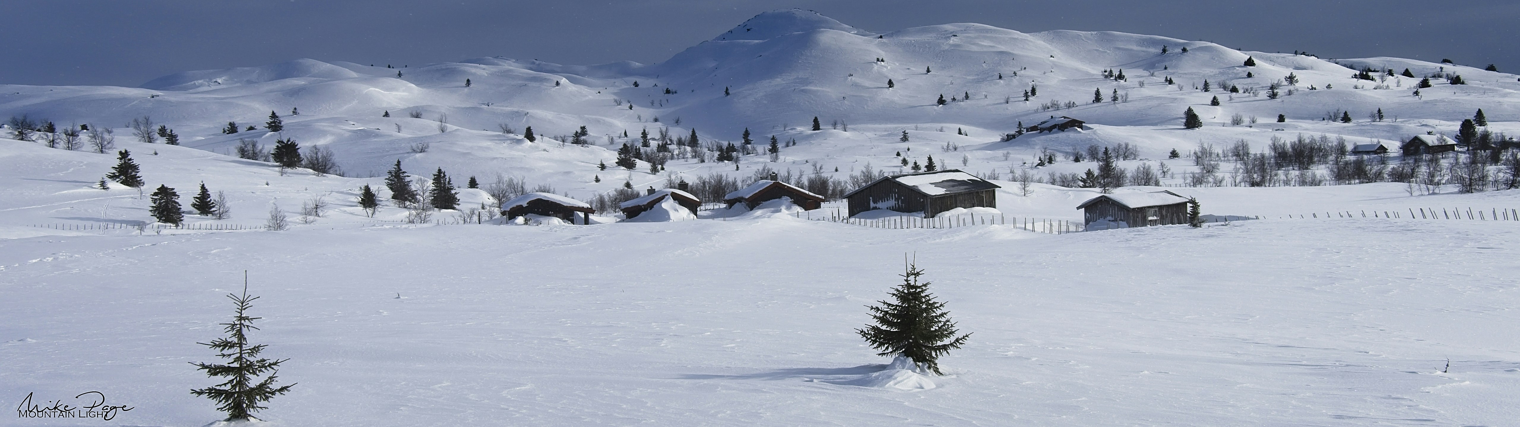 Snødekte fjell, grantrær og hytter i norsk vinterlandskap