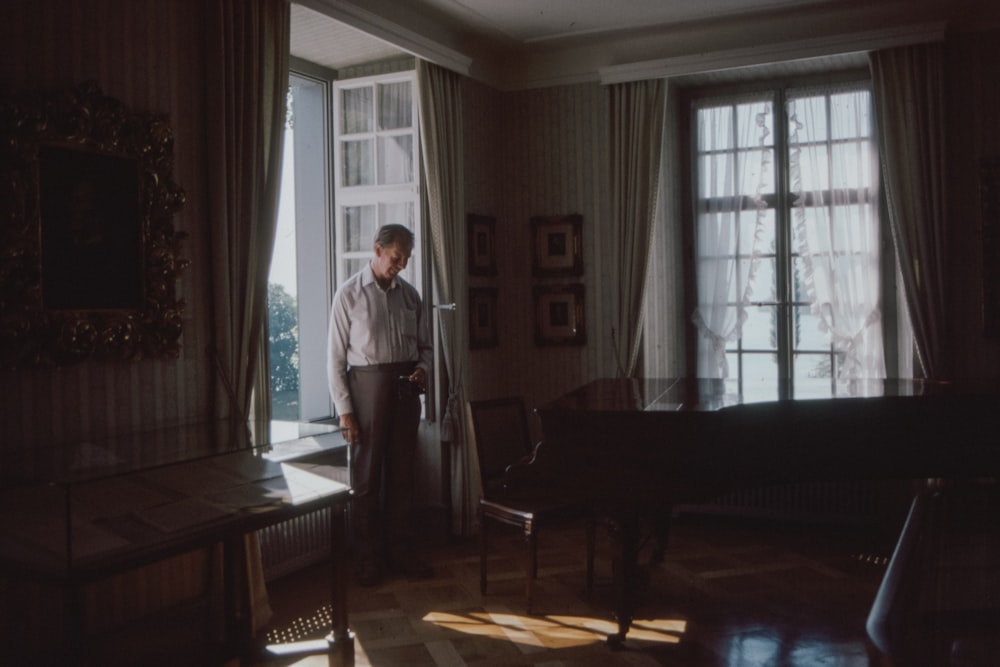 man in white shirt standing near brown wooden piano