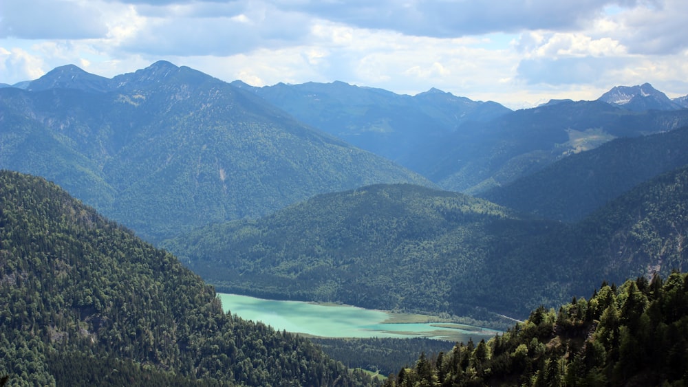 green mountains near lake under white clouds and blue sky during daytime