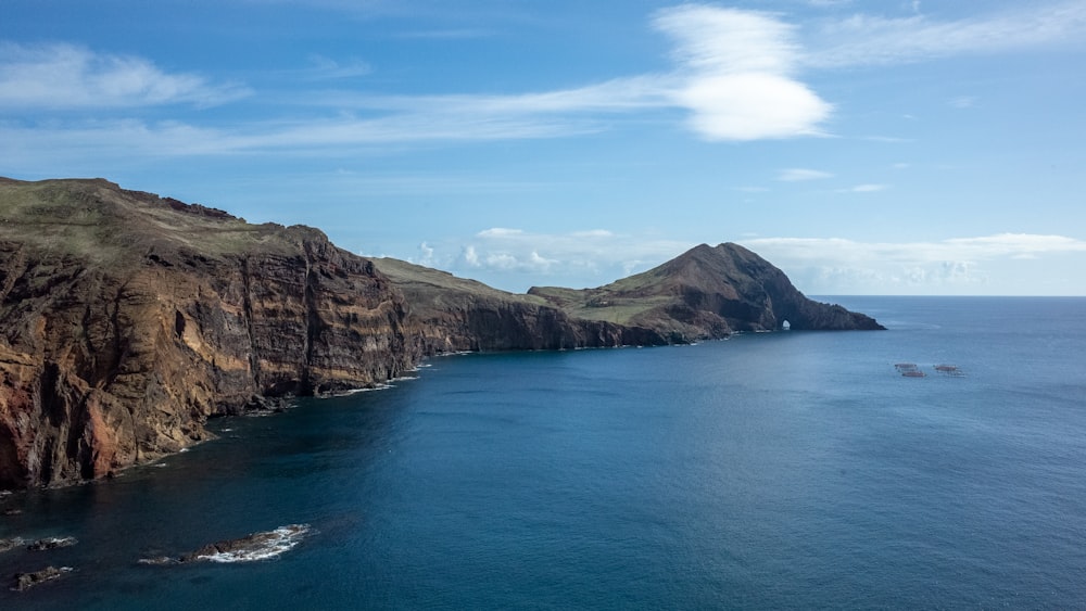 brown and green mountain beside blue sea under blue sky during daytime