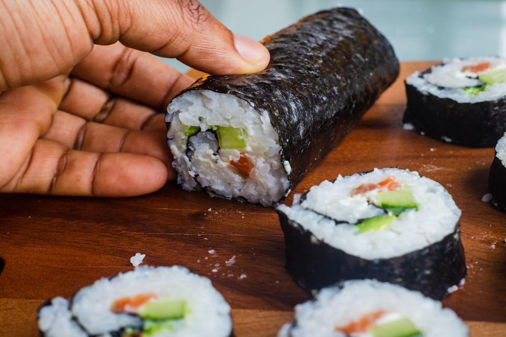 person holding sushi roll on brown wooden table