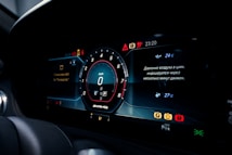 A digital car dashboard displaying various information including a speedometer set at zero, temperature readings, warning indicators, and status messages in Russian. The design is modern with illuminated icons and symbols.