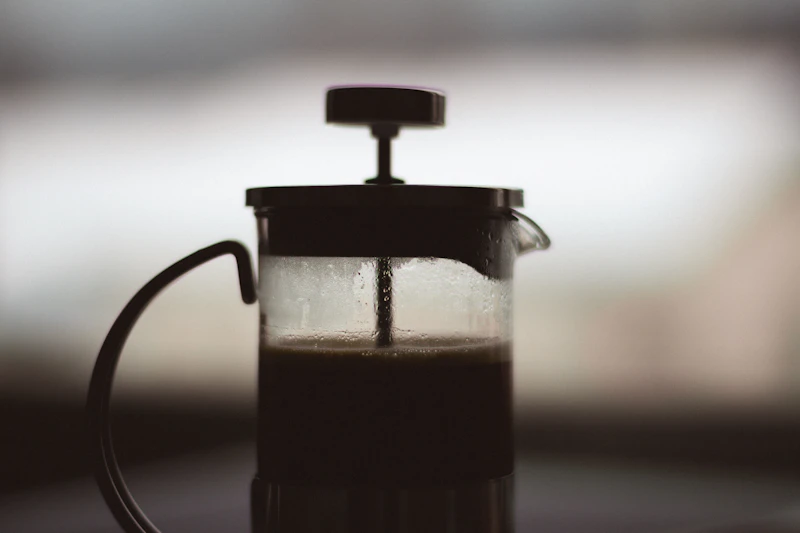 French press coffee brewer backlit on a kitchen counter