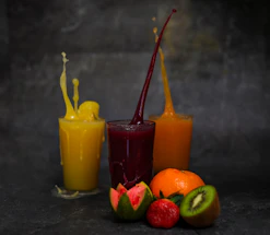 A vibrant juice glass with fresh fruits around it on a colorful background.