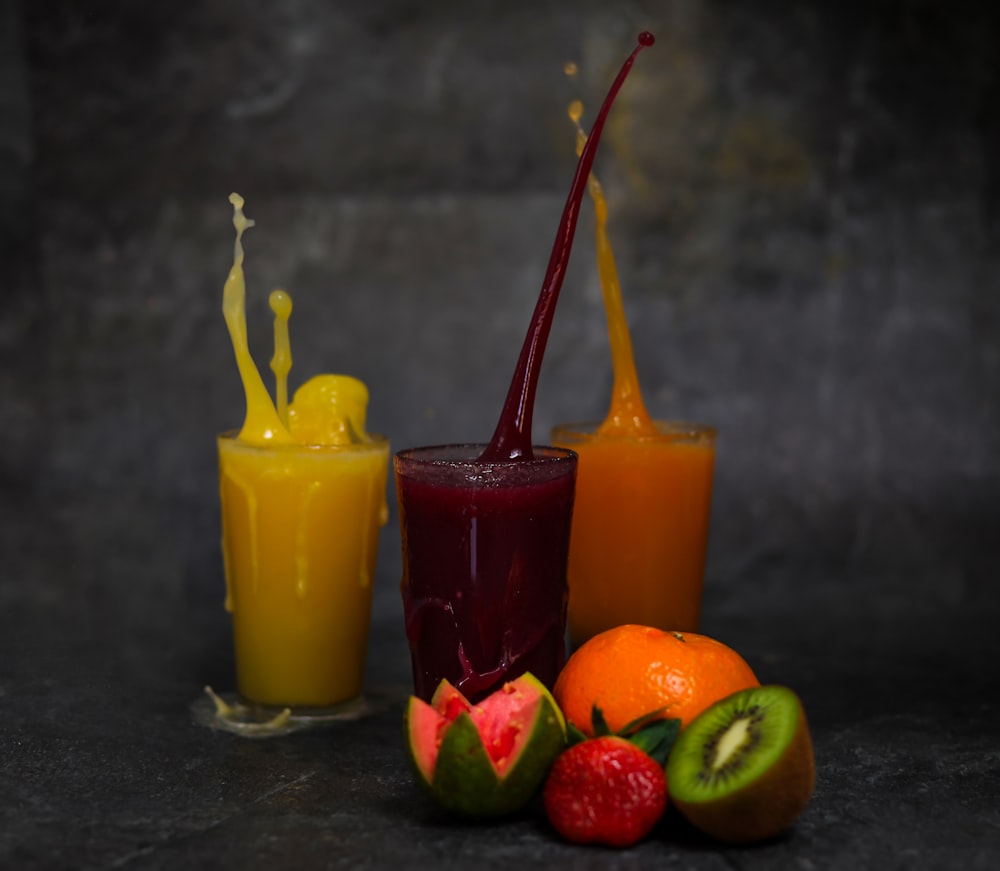 three yellow orange and green juice in clear drinking glasses