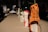 A row of objects placed on a tabletop, each wrapped in a unique material such as an orange rubber material with some text and diagrams on it. The setting appears to be indoors with a dimly lit environment and blurred figures in the background.
