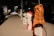 A row of objects placed on a tabletop, each wrapped in a unique material such as an orange rubber material with some text and diagrams on it. The setting appears to be indoors with a dimly lit environment and blurred figures in the background.