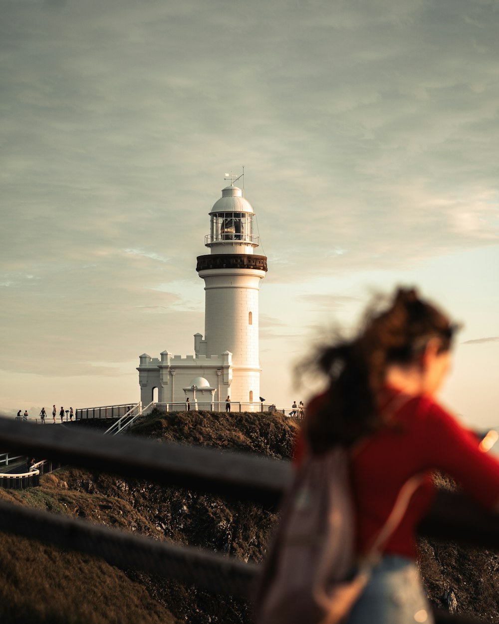 woman in red jacket standing near white lighthouse during daytime