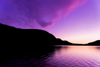 A serene lakeside view reflecting the vibrant colors of a sunset behind a mountain range.