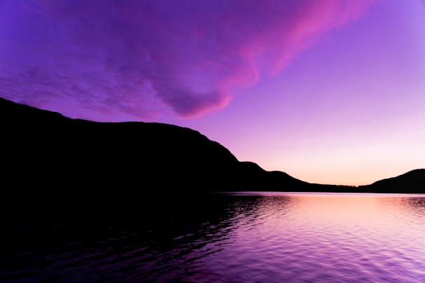 A serene lakeside view reflecting the vibrant colors of a sunset behind a mountain range.