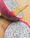 Close-up of a sliced dragon fruit with vibrant pink skin and white flesh speckled with black seeds.