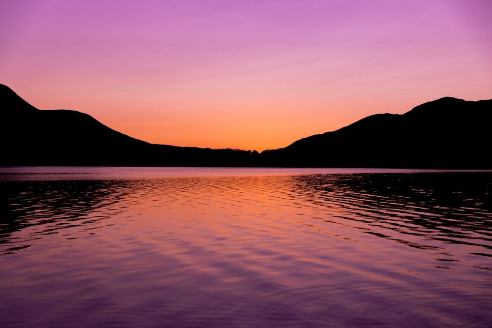 silhouette of mountain near body of water during sunset