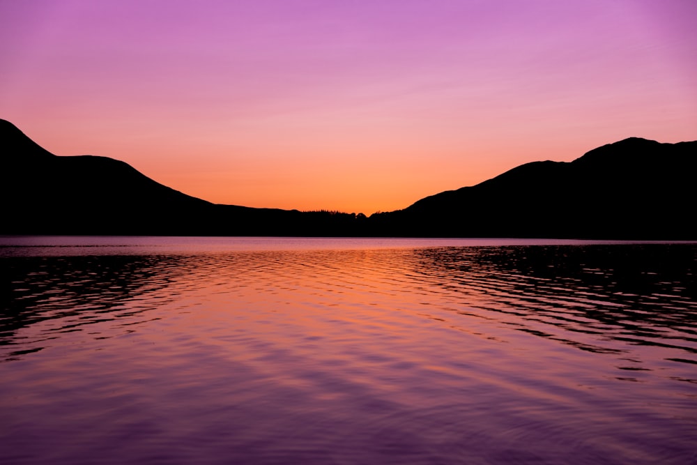 silhouette de montagne près du plan d’eau au coucher du soleil