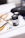 Various art supplies are arranged on a white surface, including black poster color jars, paintbrushes with orange handles, and an eraser. The background is softly blurred, indicating a creative workspace.