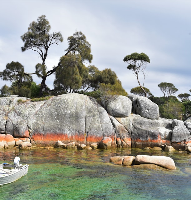 white and blue boat on body of water near gray rock formation during daytime