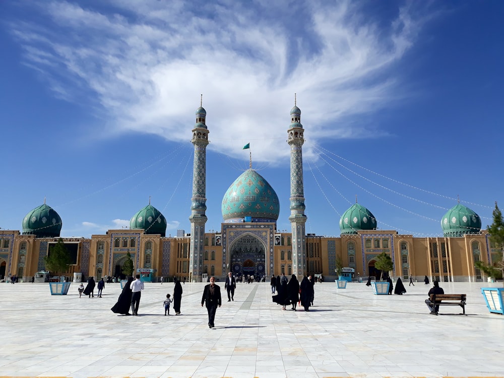 people walking on street near mosque under blue sky during daytime