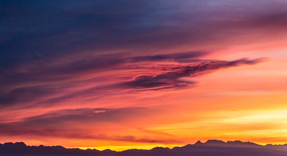 silhouette of mountains under cloudy sky during sunset