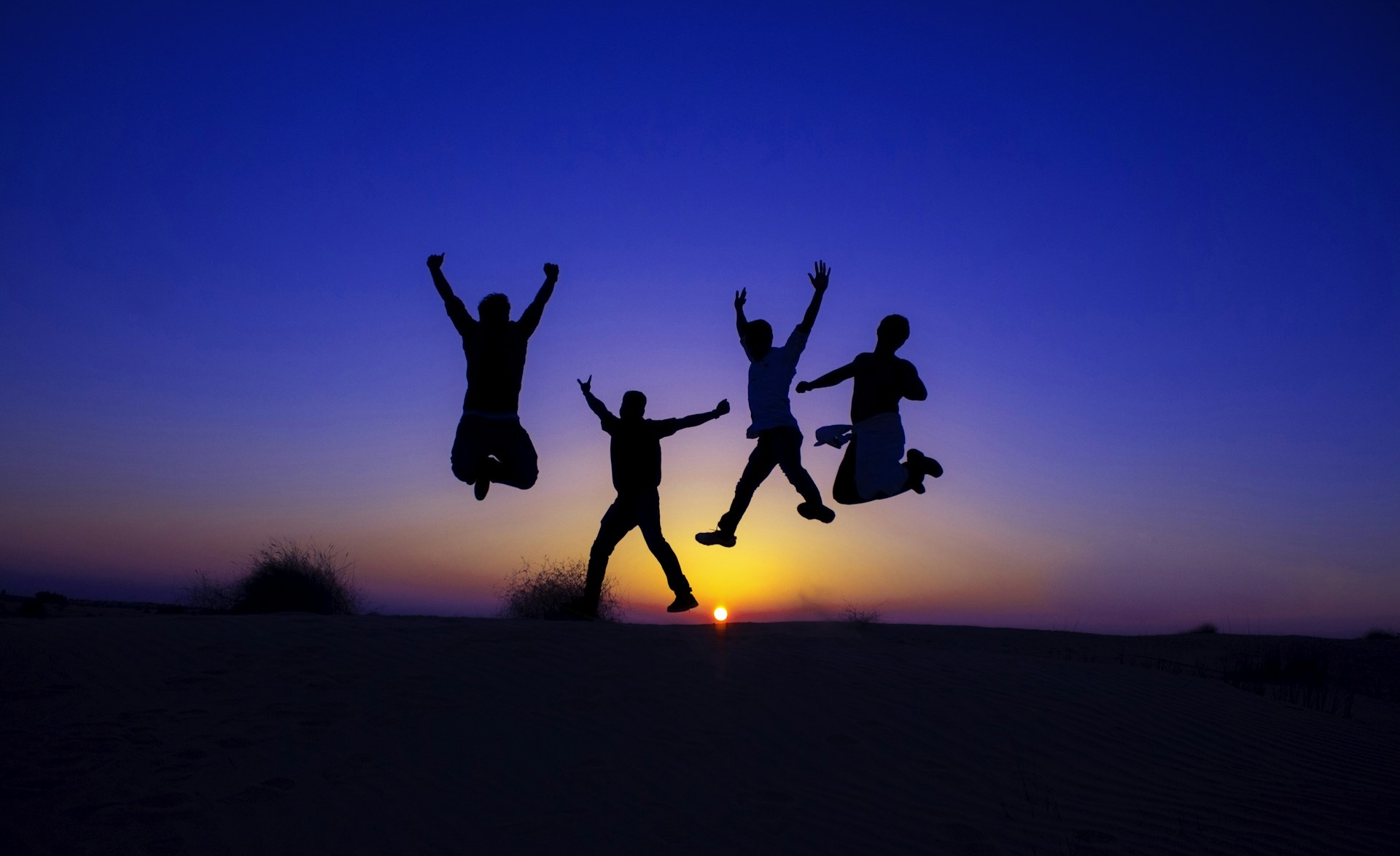 silhouette of 2 men jumping on field during sunset