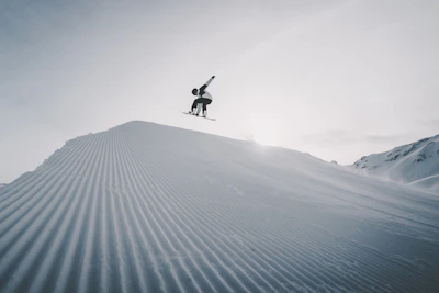 A snowscoot rider catching air over a snowy Crans-Montana slope during golden hour.