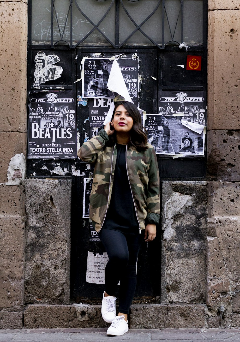 woman in green jacket and black pants sitting on black concrete wall