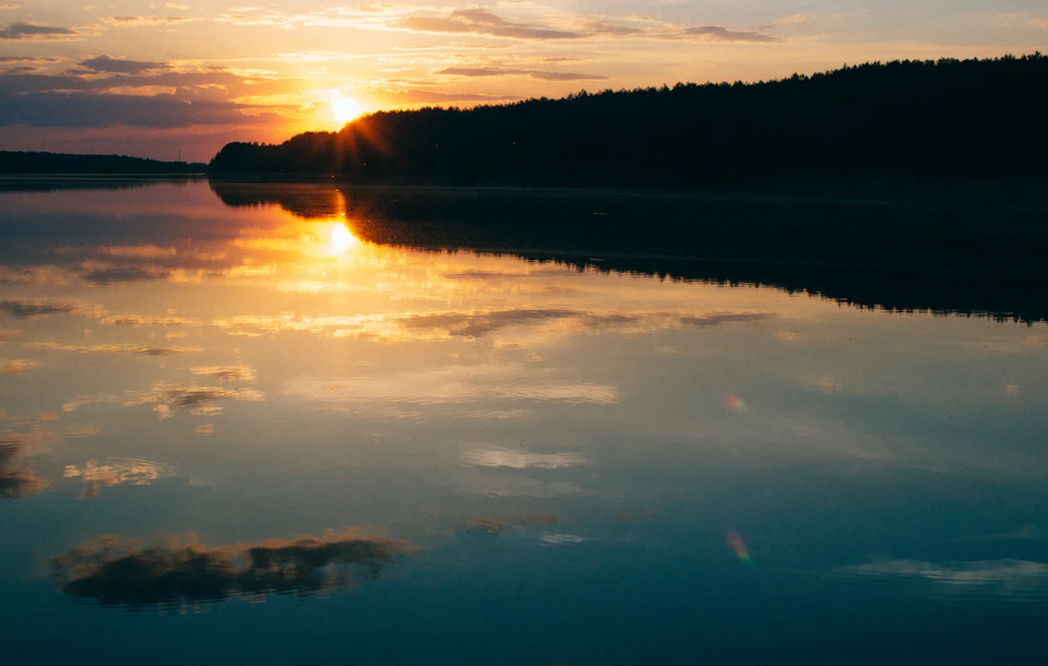 Serene sunset over calm lake with warm glow reflected on its surface