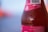 Close-up of a chilled pink lemonade bottle with condensation droplets on a sunny wooden table.