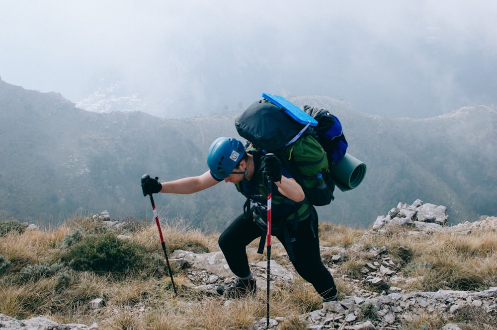 man in blue jacket and black pants with blue backpack standing on rocky ground during daytime