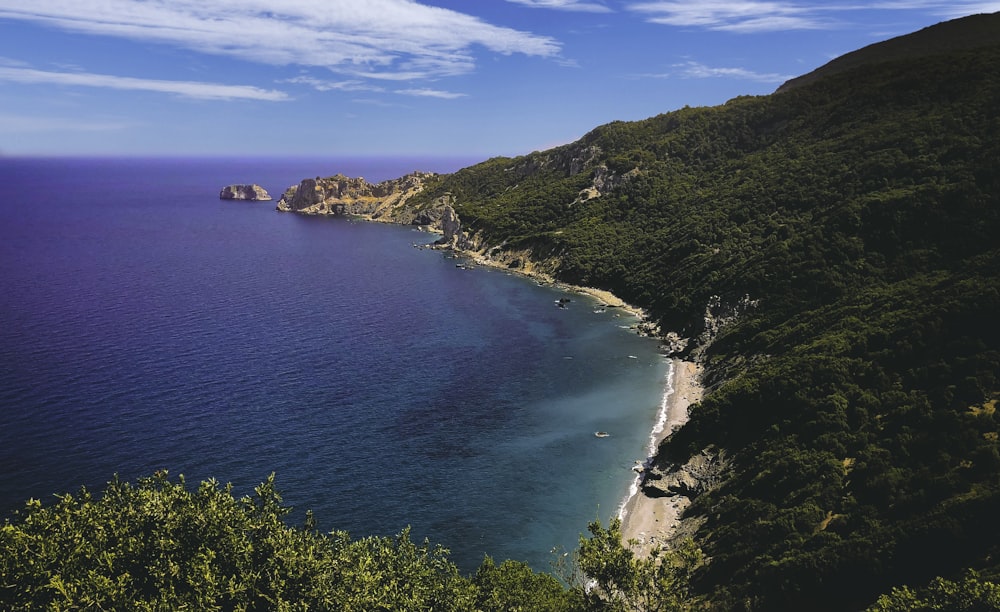 Montagna verde accanto al mare blu sotto il cielo blu durante il giorno