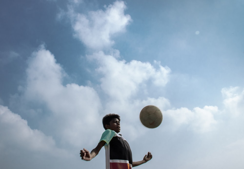boy in green and white shirt holding yellow ball under blue and white sunny cloudy sky