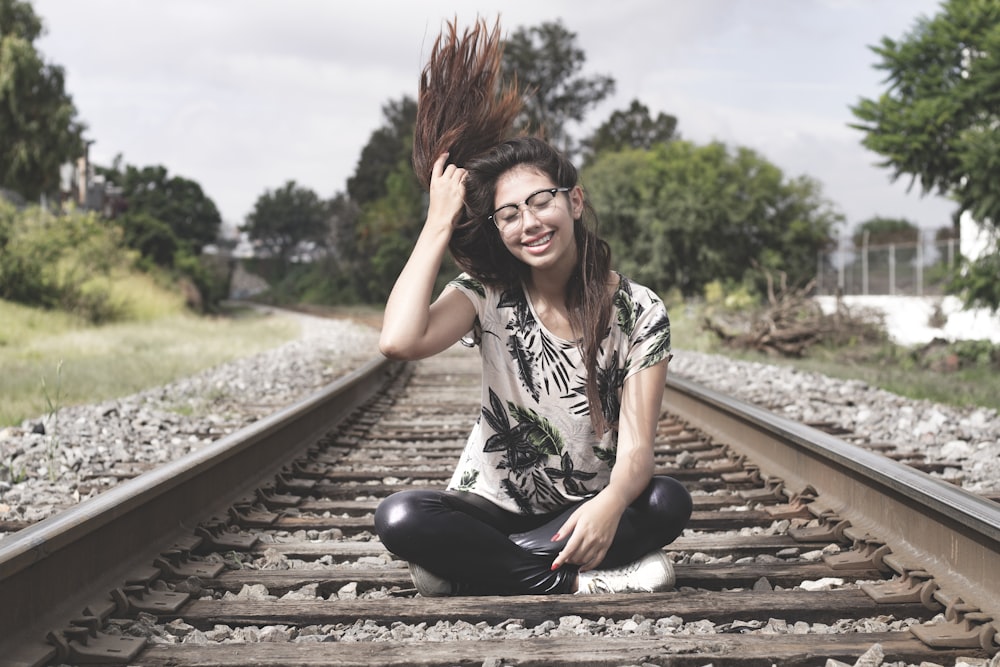 woman in white and black floral shirt and black pants sitting on train rail during daytime