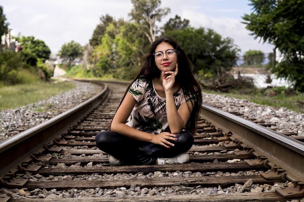 woman in black and white floral shirt and black pants sitting on train rail during daytime