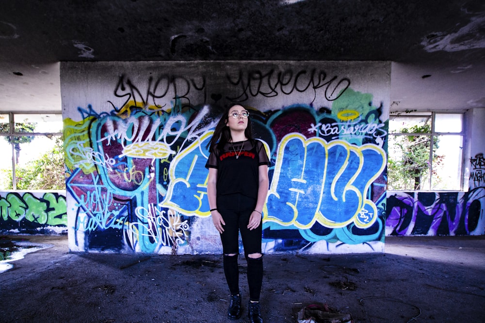 woman in black jacket standing beside wall with graffiti