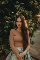 woman in brown long sleeve shirt standing near green tree during daytime