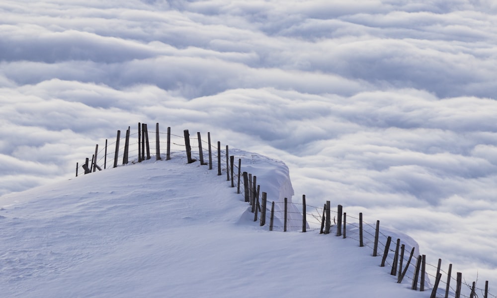 Recinzione di legno marrone su terreno coperto di neve sotto nuvole bianche e cielo blu durante il giorno