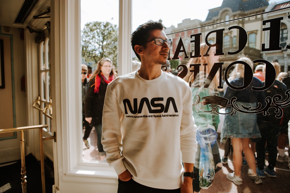 man in white and black sweater standing near glass window