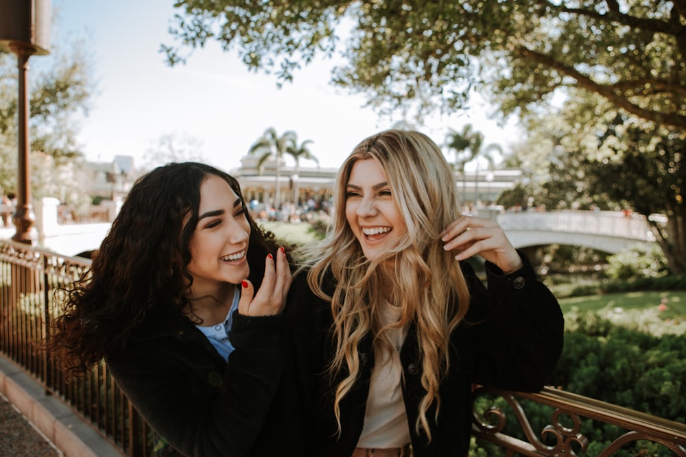 2 women smiling and standing near trees during daytime