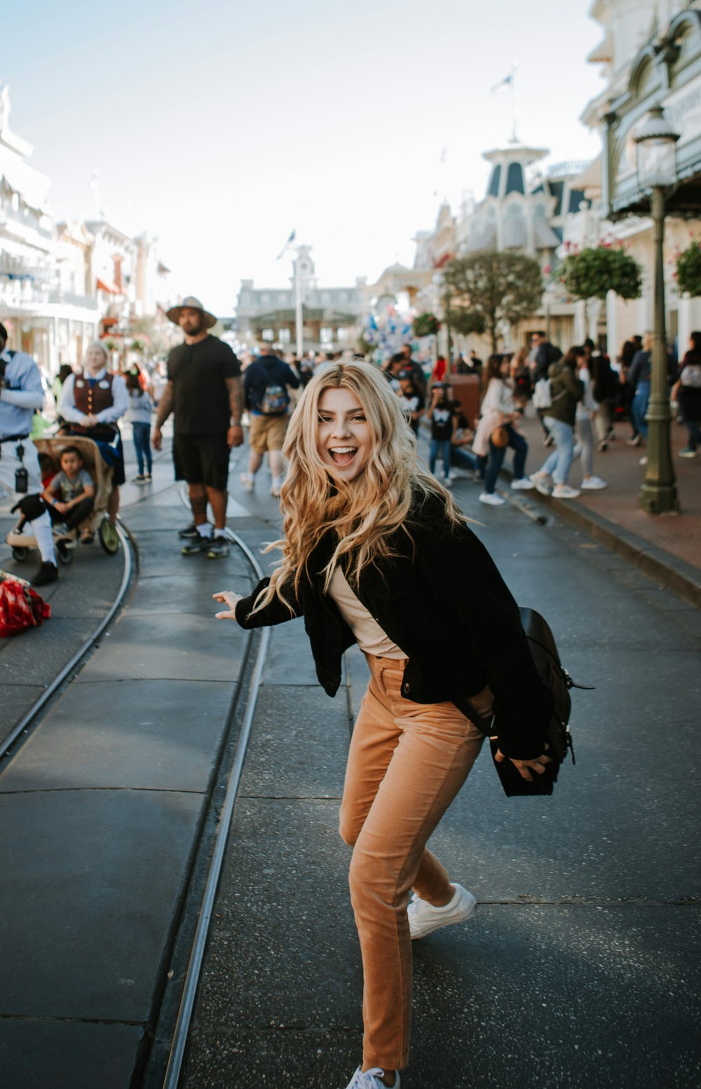 woman in black jacket and brown pants standing on sidewalk during daytime